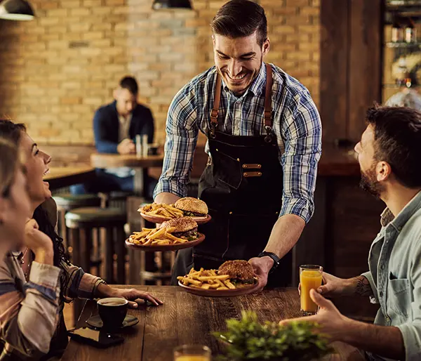 Serveur qui sert des plats à un groupe d'amis dans restaurant en contrat de concession.