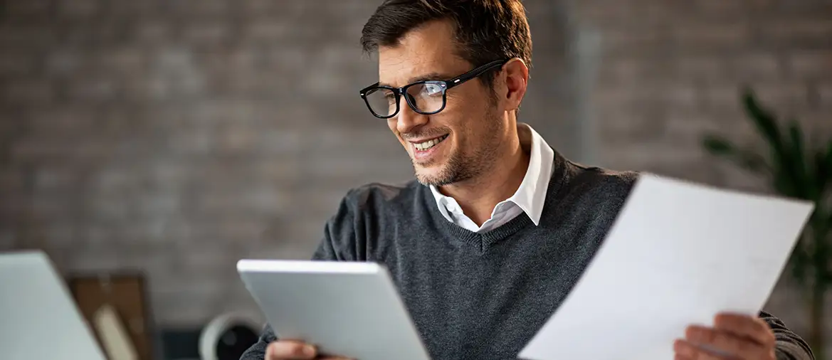 Un franchiseur qui a des obligations pour son réseau de franchises. Il tient une tablette et un papier en regardant son ordinateur portable.